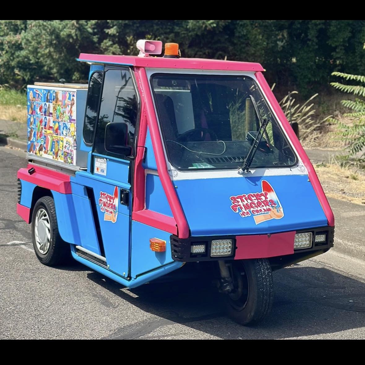 A Sticky Fingers pink and blue scooter ice cream truck parked in the sun